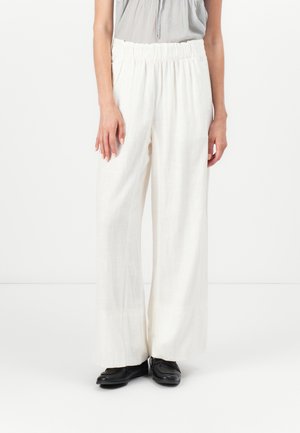 Witte, wijde broek met een elastische tailleband, gemaakt van lichtgewicht stof. Gepaard met zwarte schoenen, wat een kleurcontrast creëert.