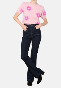 Suéter corto de manga corta color rosa claro con apliques de flores rosas, combinado con jeans de tiro alto acampanados azul oscuro y botines negros.