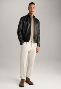 Veste en cuir noire avec un col haut, haut en tricot beige, pantalon blanc ajusté et bottines en suède brun. Texture lisse et coupe sur mesure.