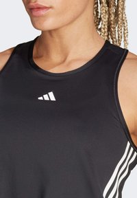 Czarny sportowy top na ramiączkach z okrągłym dekoltem, z białym logo Adidas i trzema pionowymi białymi paskami po bokach. Gładki, elastyczny materiał.