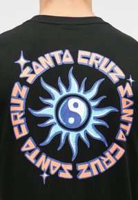 Mustakarva särgil on keskel sinine päike ja jin-jang sümbol, mida ümbritseb stiliseeritud oranž kirjas "Santa Cruz".