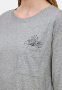 Szara bawełniana koszulka oversize z kieszonką na piersi, ozdobiona czarnym kwiatowym konturem. Miękka tekstura i luźny krój.