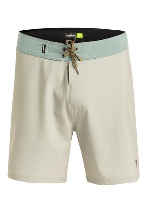 Ljust beige simbyxor med midjeband i mintgrön färg, snörning i midjan och en liten logotyp på den nedre sidan. Slät textur.