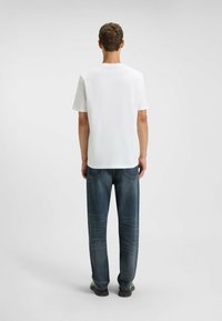 Witte korte mouwen t-shirt gezien vanaf de achterkant, gecombineerd met donkerblauwe jeans. Casual pasvorm met een gladde textuur en een minimalistisch ontwerp.