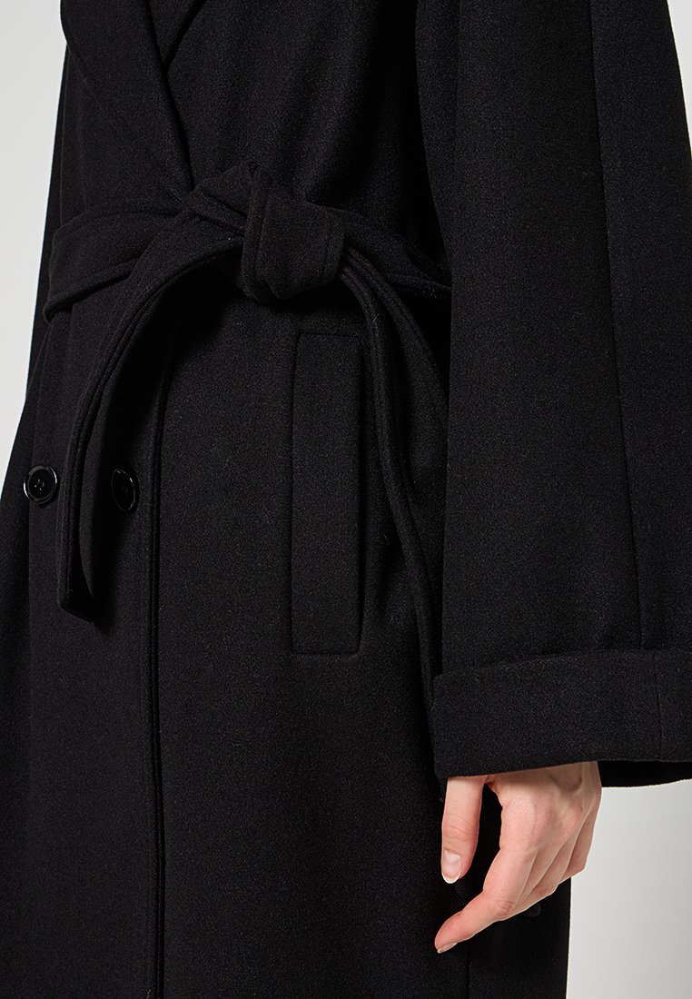 Czarny wełniany płaszcz z paskiem, dużymi kieszeniami z przodu i strukturalnym krojem. Cecha gładka tekstura i zapinane mankiety.