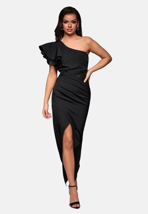 Musta olkaimeton mekko, jossa on röyhelöyksityiskohta, tiukka bodice, teksturoitu verkko-osa vyötäröllä ja reiden ylle ulottuva halkio lisädramaa varten.