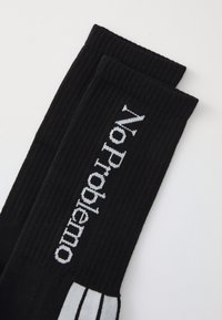 Black ribbed socks featuring the text "No Problemo" in white stitching. Accented with three white stripes at the top.