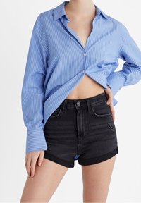 Chemise boutonnée à rayures bleues claires avec une coupe décontractée, associée à un short en denim noir taille haute avec revers et un effet usé.