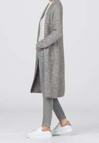 Person wearing long gray fuzzy cardigan, white turtleneck, gray skinny jeans, and white sneakers with beige accents, standing sideways.