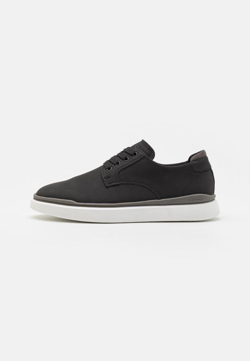Chaussure noire à lacets avec une tige lisse mate, des accents en mesh texturé et une semelle en caoutchouc blanche. Caractérisée par un bout arrondi et un marquage minimal.