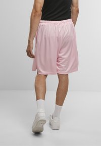Lyserøde sportsshorts med elastisk talje, lavet af letvægtsstof. Båret med hvide sneakers og ribbede ankelstrømper.