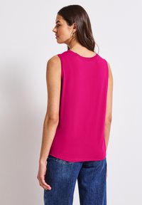 Top senza maniche fucsia con scollo rotondo e cuciture decorative. Abbinato a jeans in denim blu, che mostrano una consistenza e una vestibilità morbide.