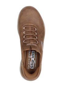 Zapatilla slip-on de textura suave en color marrón con detalles de cordones elásticos, plantilla acolchada y suela de goma blanca translúcida. Incluye logo en el costado.