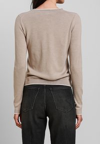 Maglione beige a maglia con maniche lunghe, scollatura rotonda e orlo a coste, abbinato a pantaloni in denim scuro con tasche posteriori e dettagli di cucitura.