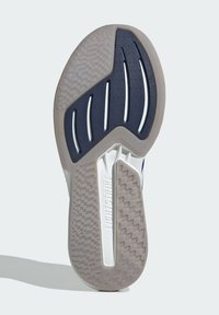 Semelle de chaussure présentant une surface en caoutchouc texturé, principalement blanche avec des accents marine, et des motifs géométriques pour la traction et le soutien.
