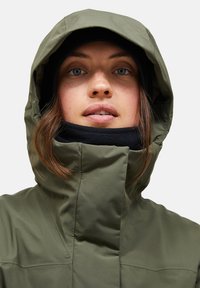 Olivgrüne wasserdichte Jacke mit hohem Kragen und verstellbarem Kapuze, über einem schwarzen Fleece-Halswärmer, der eine glatte Textur zeigt.