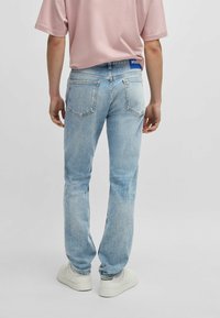 Jeans de mezclilla azul claro con un corte recto, diseño de cinco bolsillos y costuras visibles. Usado con una camiseta rosa pálido y zapatillas blancas.