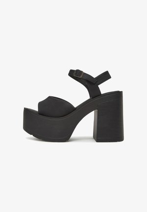 Sandalias de plataforma negras con tacón grueso, que cuentan con una correa ancha y hebilla ajustable en el tobillo. Material suave y diseño de punta redondeada.