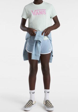 Jasnozielona koszulka Vans z krótkim rękawem i różowym logo, zestawiona z jasnoniebieskimi szortami i trampkami Vans w wzór szachownicy.