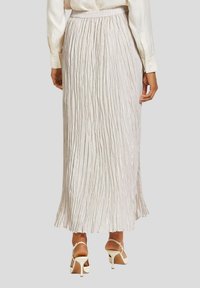 Plissé maxi rok in lichtbeige, met een elastische tailleband. Gelaagd, vloeiend ontwerp met brede zoom en subtiele glans. Gecombineerd met witte hakken.