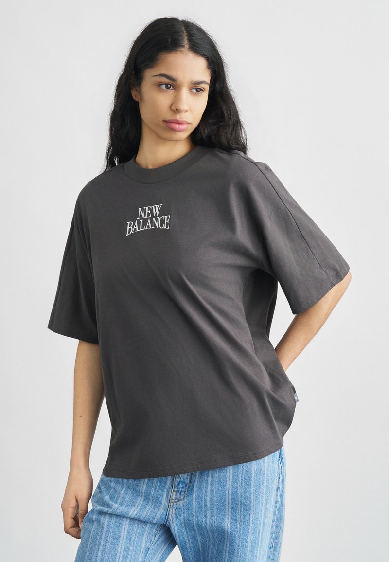 Γκρι, υπερμεγέθη βαμβακερό T-shirt με κοντά μανίκια, με κεντημένο λογότυπο "NEW BALANCE" στο μπροστινό μέρος. Συνδυάζεται με ανοιχτό μπλε τζιν.