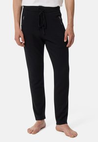 Schwarze Jogginghosen aus weichem Material mit einem Kordelzugbund, seitlichen Reißverschlusstaschen und einem dezenten Logodetail am Bein.