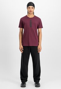 Marron t-shirt med sort "ALPHA" print, parret med løse sorte bukser. Outfittet har et enkelt design og en afslappet pasform.