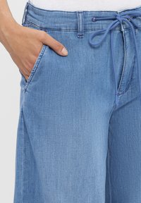Lichtblauwe denim broek heeft een trekkoord in de taille, zijzakken en een gladde textuur met subtiele kleurvariaties.