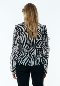 Schwarz-weiße Zebra-Print-Bluse mit Rüschensleeves und taillierter Taille. Durchscheinender Stoff mit glatter Textur und fließendem Design.