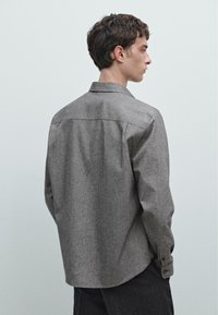 Camicia grigia in tessuto intrecciato con una texture morbida, maniche lunghe e colletto a punta. Presenta polsini con bottone e orlo curvo.