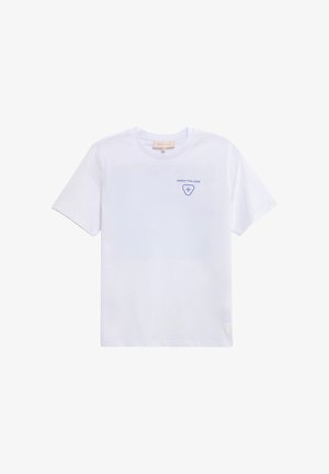 T-shirt blanc à manches courtes avec petit texte bleu “GERTRUDE” et emblème en forme de croix sur le haut gauche de la poitrine, col rond.