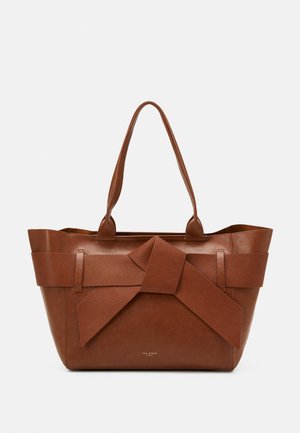 Brun læder tote taske med stor dekorativ sløjfe foran og dobbelte håndtag, Ted Baker-logo i små guld bogstaver under sløjfen.