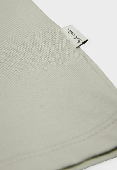 Tejido de ribete gris claro con una textura suave y un borde cosido, que presenta una pequeña etiqueta blanca en la esquina con texto negro.