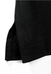 Tissu tricoté noir avec un détail de fente latérale et des coutures renforcées à l’ourlet, montrant la texture et le tissage du tissu en gros plan.