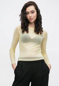 Transparante top met lange mouwen in bleekgeel, met een aansluitend ontwerp en een gladde textuur, gecombineerd met zwarte, op maat gemaakte broeken.