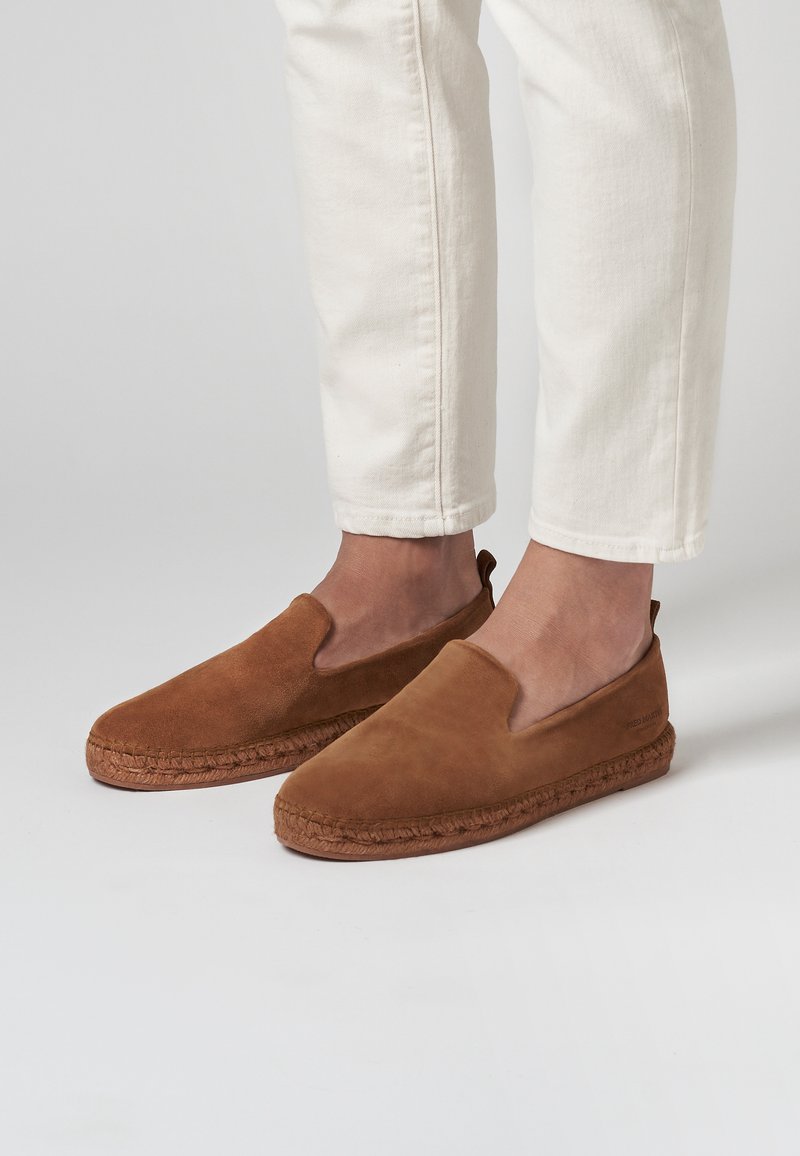 Chaussures à enfiler en suède brun avec une semelle en jute tissée, dotées d'un dessus lisse et de côtés élastiques pour un enfilage facile.