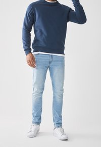 Sudadera azul marino con cuello redondo y puños acanalados, combinada con vaqueros ajustados azul claro y zapatillas blancas. Diseño sencillo y limpio.