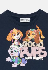 Tumši zila sporta džemperis ar karikatūru suņu rakstzīmēm, mirdzošu uzrakstu "GOOD PUPS" un "PAW PATROL" etiķeti. Mīksts audums un apaļš kakla izgriezums.