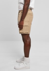 Shorts cargo beiges en tissu léger, avec une taille élastique à cordon de serrage, des poches latérales et une coupe décontractée classique.