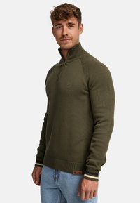 Olijfgroene zip-up trui met ribbelstructuur, getailleerd ontwerp en contrasterende gestreepte manchetten. Bevat een klein logo op de borst.