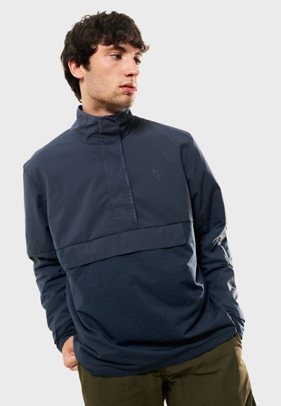 Marinblå tröja med hög krage, delvis dragkedja och texturerade paneldetaljer. Har en logotyp på bröstet och lös passform.