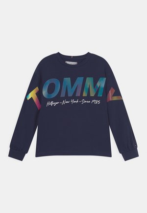 Chemise à manches longues bleu marine avec grand texte multicolore "TOMMY" et petit texte blanc "Hilfiger New York Since 1985" à l'avant.