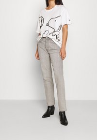 Camiseta blanca con un gráfico negro de Snoopy, combinada con unos pantalones vaqueros rectos de color gris claro y botas de tacón negras. Diseño simple y casual.