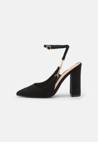 Svart mocka högklackad pumpsko med spetsig tå, ankelrem och detalj i guldkedja. Kraftig fyrkantig klack för stabilitet och stöd.