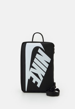 Zwarte rechthoekige Nike-tas met grote witte Swoosh en de tekst "NIKE", bovenhandvat en afneembare schouderriem op witte achtergrond.