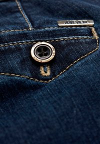 Un tissu en denim bleu foncé avec un bouton doré et un fil noir, portant l'inscription "MEYER" gravée sur le bouton et un détail de couture contrastée.