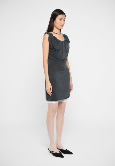 Vestido cinza escuro com decote franzido e saia ajustada, sobreposta a uma roupa interior com rendas. Usado com sapatos de salto agudo pretos.