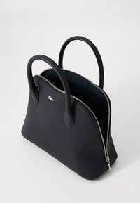 Sac fourre-tout noir en matériau synthétique texturé avec fermeture éclair. Il dispose de deux poignées arrondies et d'un logo discret sur le côté.