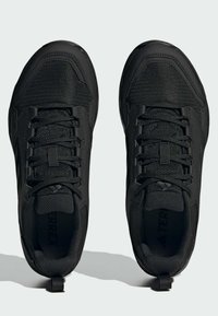 Zapatos deportivos negros con parte superior de malla, superficie texturizada y cordones planos. Presenta una puntera reforzada y una lengüeta en el talón.