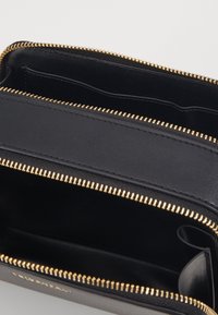 Portafoglio in pelle nera con zip dorata, dotato di molteplici scomparti e una superficie liscia. Tasche interne per carte e banconote.